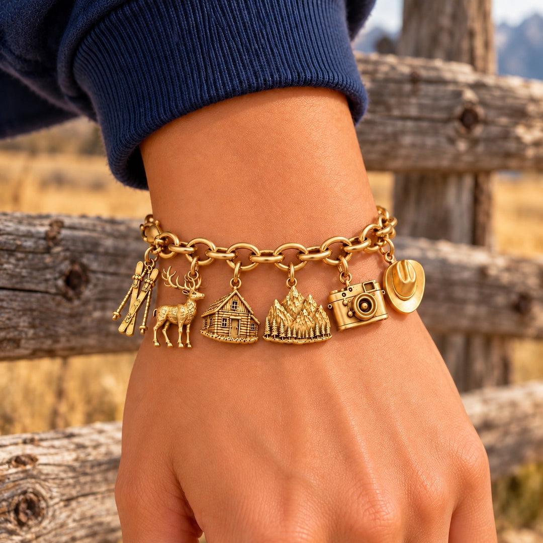 The Jackson Hole Bracelet, a gold charm bracelet worn on the wrist against a weathered split-rail fence